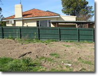 Photo of a vacant block of land and the wall of a house on the adjacent block.