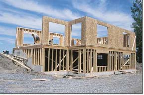 Photo of a timber house frame of a residential building with timber panels erected on the first floor. There is a pile of earth and scattered timber pieces around the site.