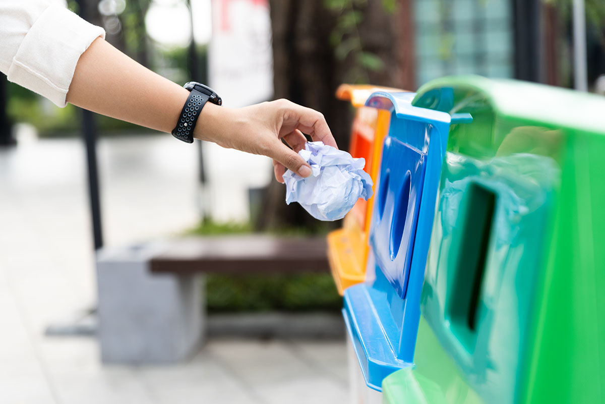 A woman's hand throwing crumpled paper in a recycling bin